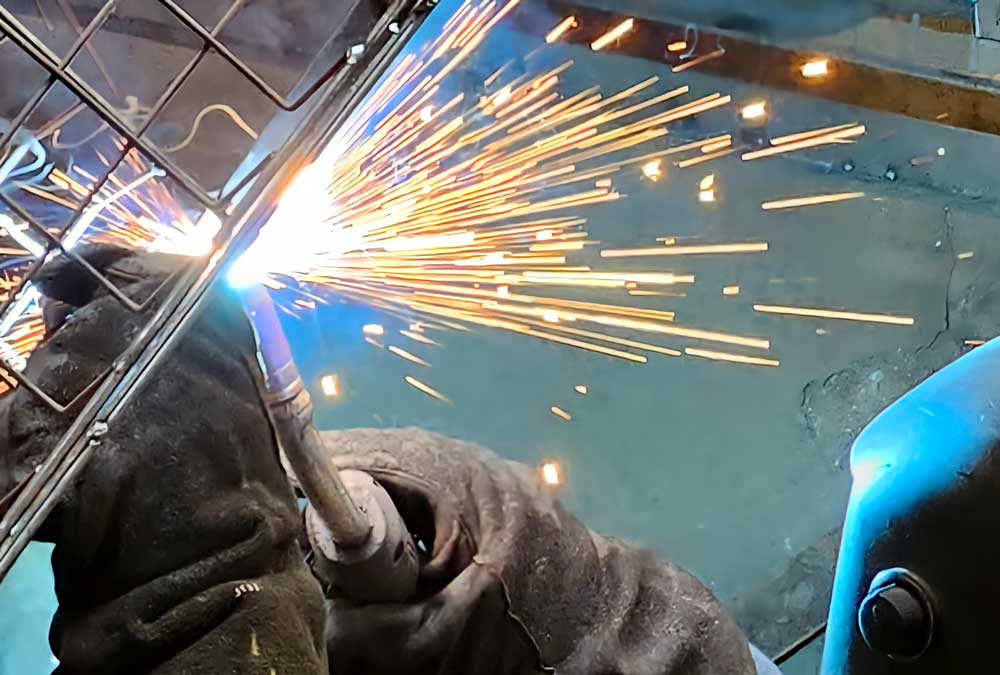 Close-up of industrial welding process with bright sparks as a worker welds a metal frame using protective gloves and torch